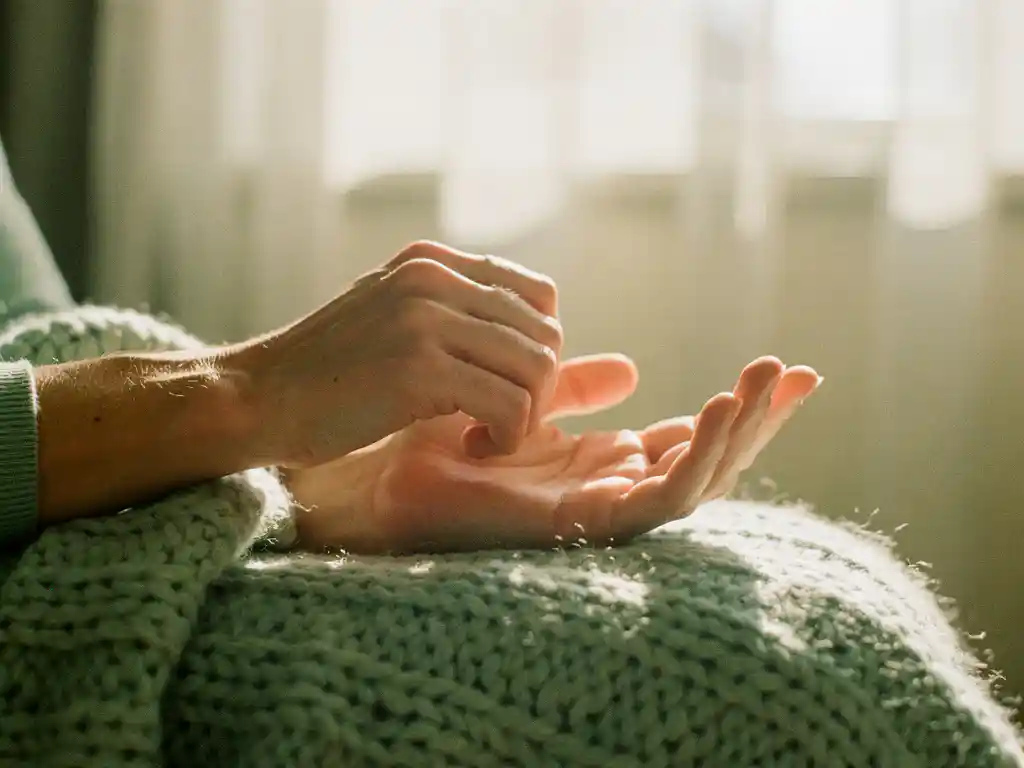 Kädet aukeavat nyrkeistä avoimiksi kämmeniksi neuletakilla, lämpimässä aamuvalossa